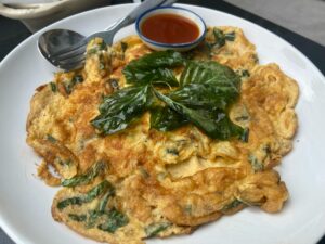 Thai-style spinach omelette with basil leaves served with spicy sauce on a white plate.
