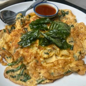 Thai-style spinach omelette with basil leaves served with spicy sauce on a white plate.