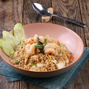 Appetizing shrimp fried rice with cucumbers in a bowl on wooden table.