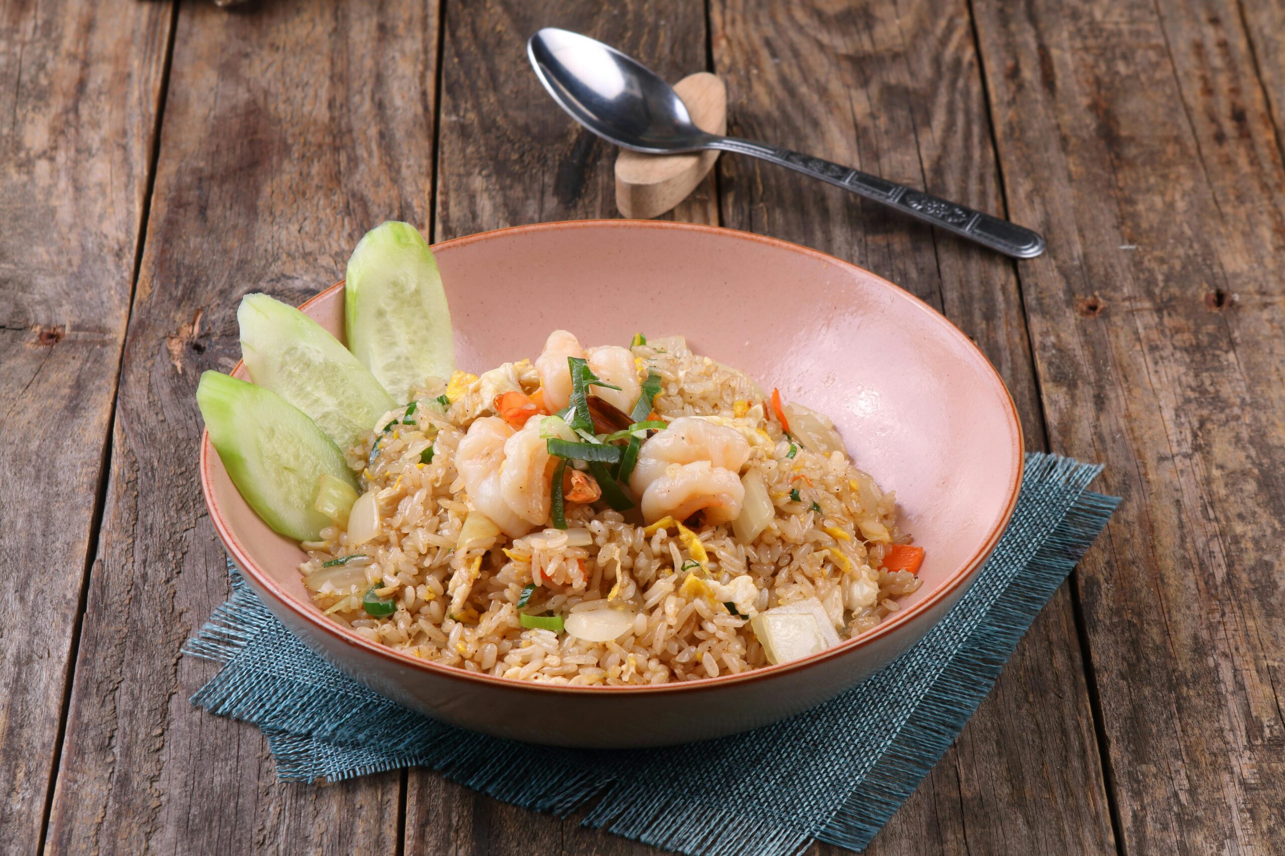 Our Menu Appetizing shrimp fried rice with cucumbers in a bowl on wooden table.