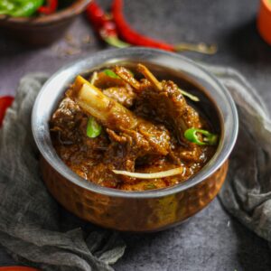 Close-up of a spicy mutton curry served in a traditional copper bowl, showcasing rich Indian flavors.