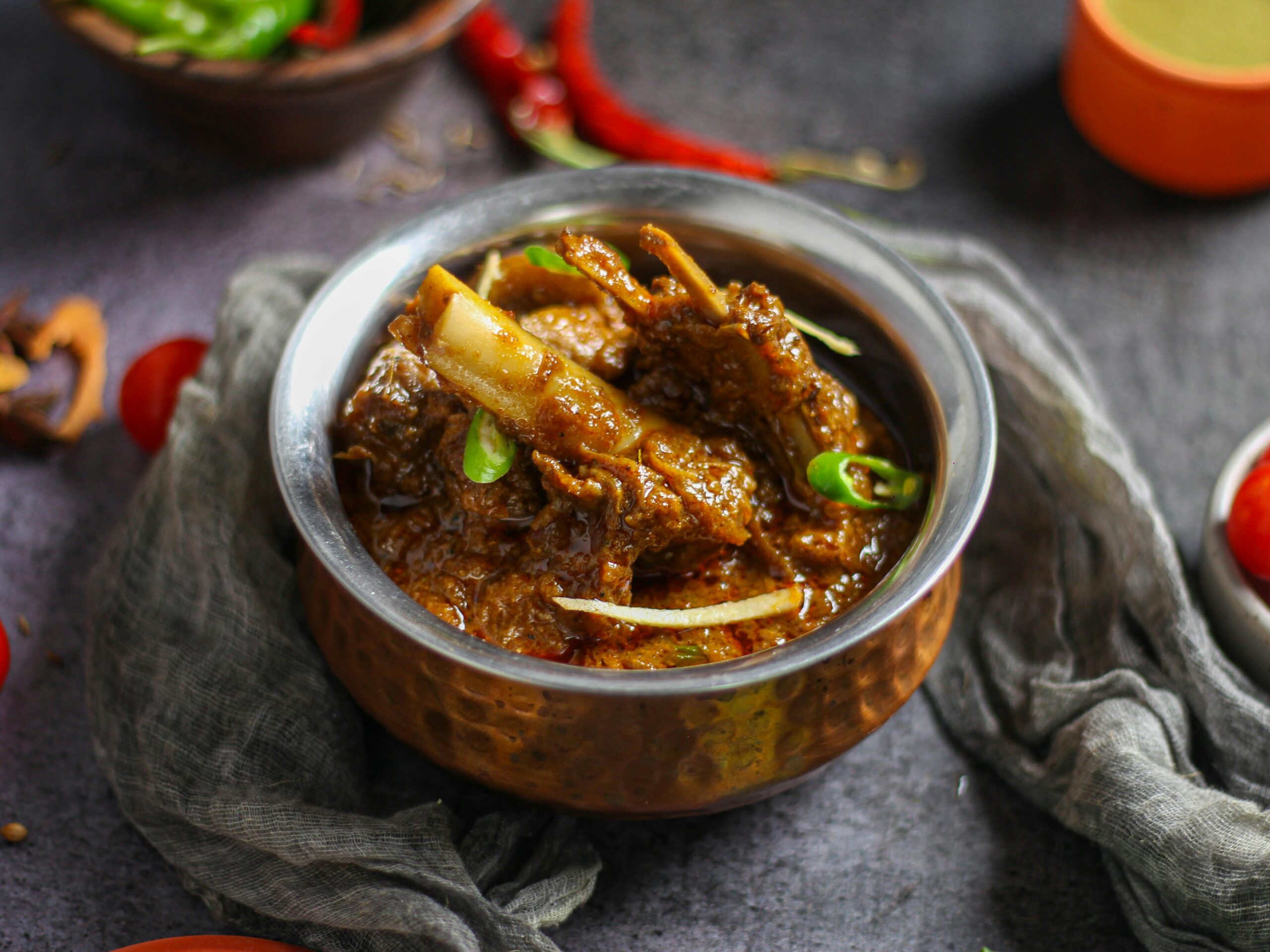 Our Menu Close-up of a spicy mutton curry served in a traditional copper bowl, showcasing rich Indian flavors.