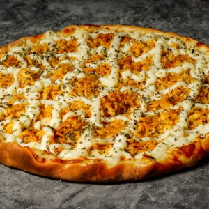 Close-up of a chicken pizza topped with herbs and cheese on a rustic surface.