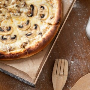 Delicious mushroom pizza with cheese in a cardboard box on a wooden table with flour.