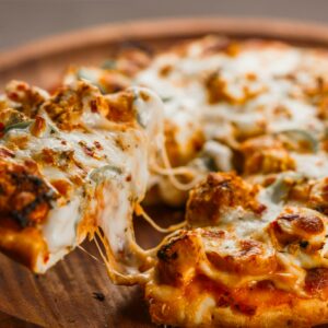 Close-up of a hot cheesy pizza being served with flavorful toppings on a wooden platter.