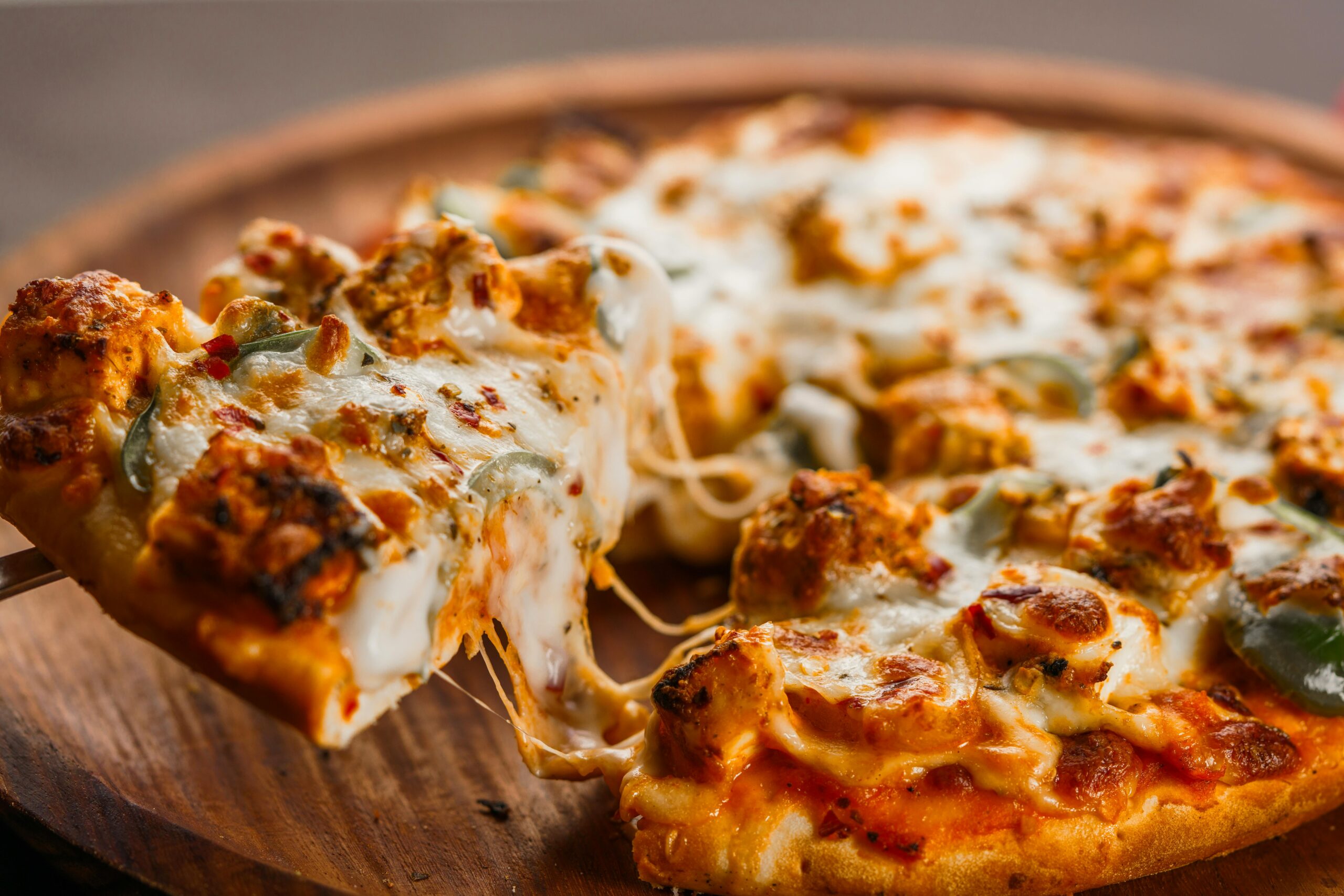 Our Menu Close-up of a hot cheesy pizza being served with flavorful toppings on a wooden platter.