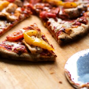 Close-up of sliced pizza with pepperoni, cheese, and bell peppers on a wooden board.